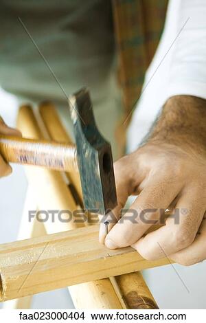 Man hammering nail into piece of wood, close-up of hands View Large Photo Image Picture - Man hammering nail into piece of wood, close-up of hands. Fotosearch
