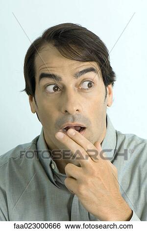 Man holding fingers in front of mouth, looking surprised, portrait View Large Photo Image Stock Photograph - Man holding fingers in front of mouth, looking surprised, portrait. Fotosearch