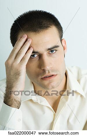 Stock Photo - Man holding head, looking at camera, portrait. Fotosearch