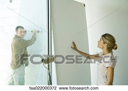Man holding level against wall and woman putting hand against wall board View Large Photo Image Stock Image - Man holding level against wall and woman putting hand against wall board. Fotosearch