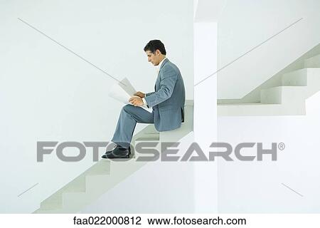 Stock Image - Man in suit sitting on stairs, looking at documents. Fotosearch