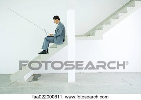 Man in suit sitting on stairs, using laptop View Large Photo Image Stock Image - Man in suit sitting on stairs, using laptop. Fotosearch