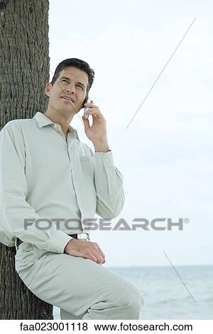 Man leaning against palm tree trunk, using cell phone, looking up View Large Photo Image Stock Photo - Man leaning against palm tree trunk, using cell phone, looking up. Fotosearch