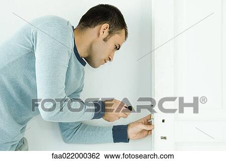 Stock Image - Man removing lock from door. Fotosearch