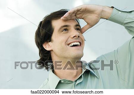 Man shading eyes, looking up, smiling, portrait View Large Photo Image Picture - Man shading eyes, looking up, smiling, portrait. Fotosearch