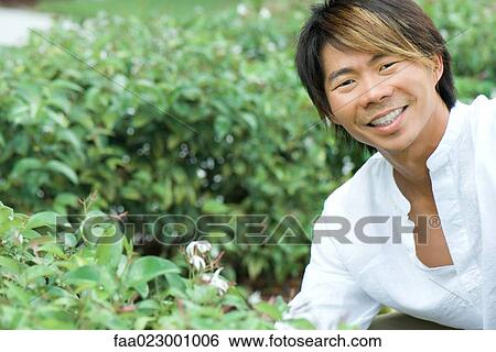 Man smiling at camera next to flowering shrub, portrait View Large Photo Image Stock Photograph - Man smiling at camera next to flowering shrub, portrait. Fotosearch