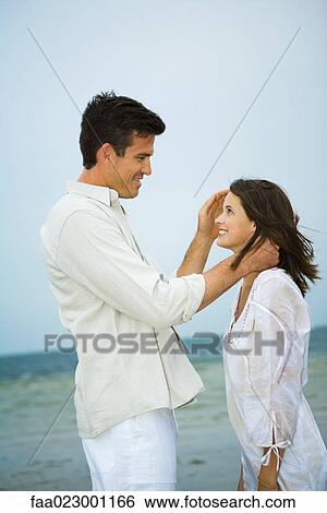 Man standing face to face with young female companion on beach, pushing her hair back, side view View Large Photo Image Stock Photograph - Man standing face to face with young female companion on beach, pushing her hair back, side view. Fotosearch