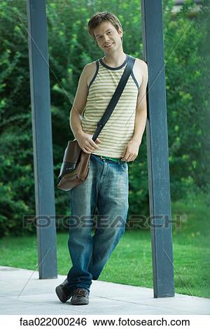 Stock Photograph - Man standing leaning against post, smiling, full length portrait. Fotosearch