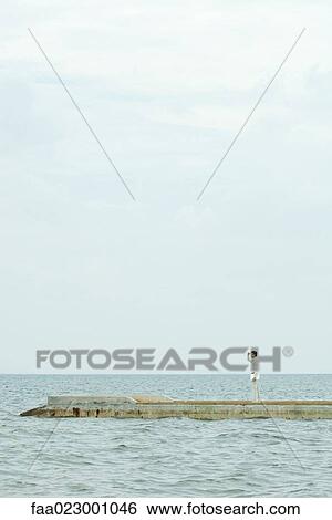 Man standing on jetty, carrying laptop computer, looking at view, shading eyes View Large Photo Image Stock Photograph - Man standing on jetty, carrying laptop computer, looking at view, shading eyes. Fotosearch