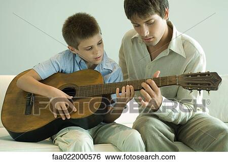 Stock Photograph - Man teaching boy to play the guitar. Fotosearch