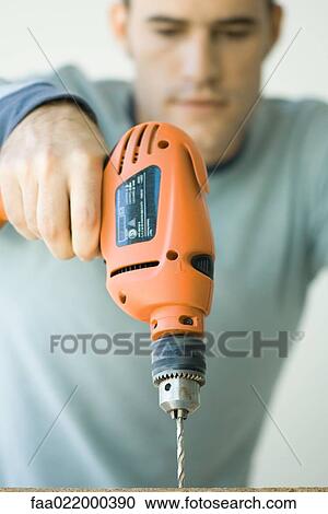 Stock Image - Man using drill, focus on drill in foreground. Fotosearch