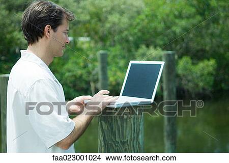 Man using laptop computer outdoors, next to lake View Large Photo Image Picture - Man using laptop computer outdoors, next to lake. Fotosearch
