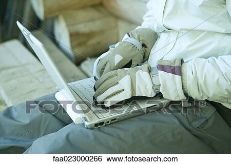 Stock Photograph - Man using laptop with gloves on. Fotosearch