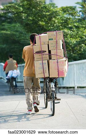Stock Photo - Man walking with bike stacked with boxes. Fotosearch