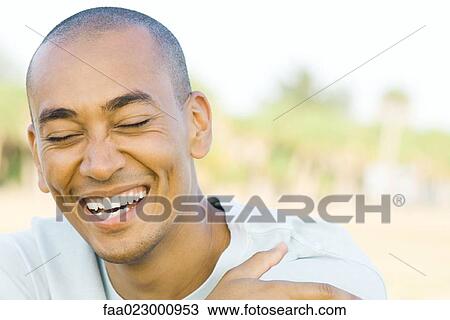 Stock Image - Man with shaved head, laughing, eyes closed, portrait. Fotosearch
