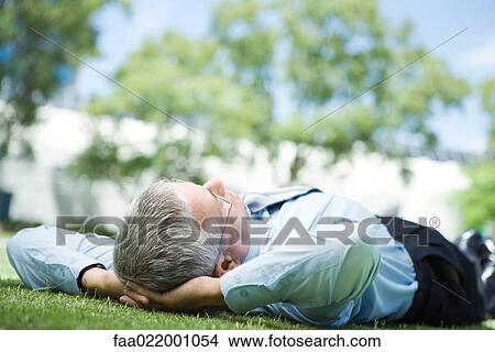 Mature businessman lying on ground outdoors, hands behind head View Large Photo Image Picture - Mature businessman lying on ground outdoors, hands behind head. Fotosearch