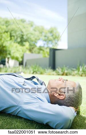 Mature businessman lying on ground outdoors, hands behind head, eyes closed, side view View Large Photo Image Stock Image - Mature businessman lying on ground outdoors, hands behind head, eyes closed, side view. Fotosearch