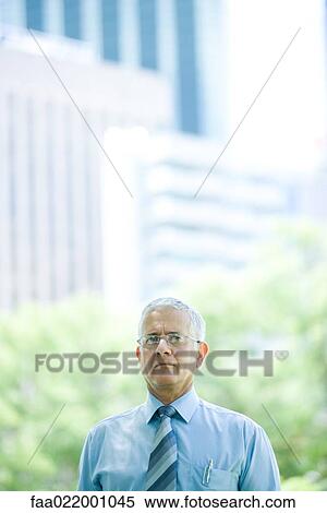 Stock Photography - Mature businessman outdoors, frowning at camera, head and shoulders. Fotosearch