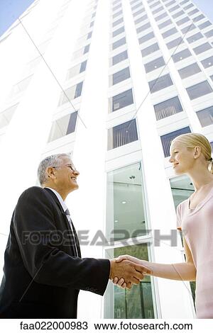 Mature businessman shaking young businesswoman's hand in front of building, low angle view View Large Photo Image Stock Image - Mature businessman shaking young businesswoman's hand in front of building, low angle view. Fotosearch