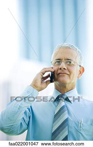 Stock Photo - Mature businessman using cell phone, smiling, front view. Fotosearch