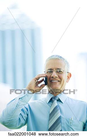 Stock Photo - Mature businessman using cell phone, smiling at camera. Fotosearch