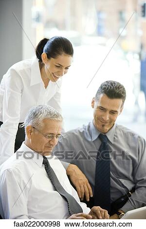 Mature businessman using laptop computer, two colleagues looking over his shoulder View Large Photo Image Stock Photo - Mature businessman using laptop computer, two colleagues looking over his shoulder. Fotosearch
