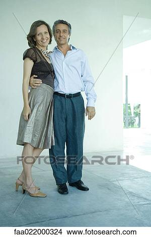 Mature couple standing together, man's arm around woman's waist, smilng at camera, full length portrait View Large Photo Image Picture - Mature couple standing together, man's arm around woman's waist, smilng at camera, full length portrait. Fotosearch