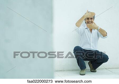 Mature man crouching, framing face with hands, smiling View Large Photo Image Stock Image - Mature man crouching, framing face with hands, smiling. Fotosearch