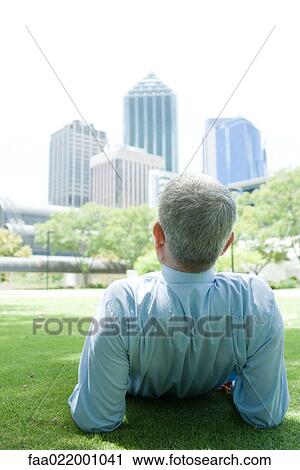 Mature man reclining on ground, looking at urban scene, rear view View Large Photo Image Stock Image - Mature man reclining on ground, looking at urban scene, rear view. Fotosearch