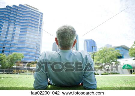 Mature man reclining on ground, looking at urban scene, rear view View Large Photo Image Stock Image - Mature man reclining on ground, looking at urban scene, rear view. Fotosearch