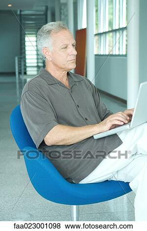 Stock Photo - Mature man sitting in chair, using laptop computer, looking away. Fotosearch