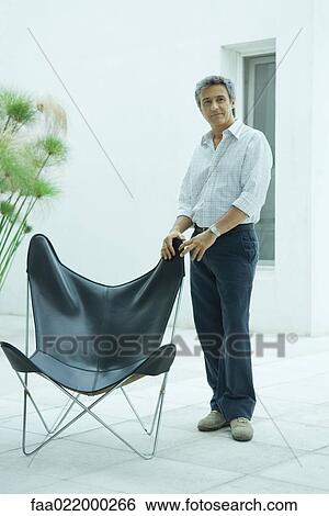 Mature man standing by chair, full length portrait View Large Photo Image Stock Photograph - Mature man standing by chair, full length portrait. Fotosearch