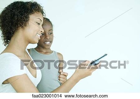 Mother and daughter looking at cell phone together, smiling View Large Photo Image Picture - Mother and daughter looking at cell phone together, smiling. Fotosearch