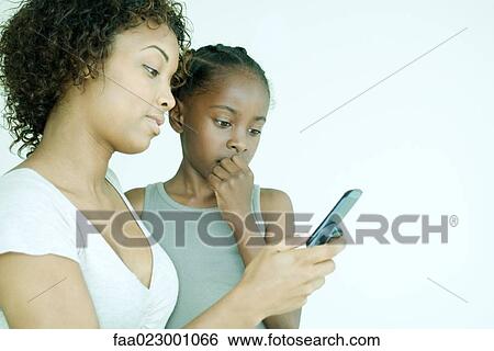 Mother and daughter looking down at cell phone together, girl's hand over mouth View Large Photo Image Stock Photograph - Mother and daughter looking down at cell phone together, girl's hand over mouth. Fotosearch