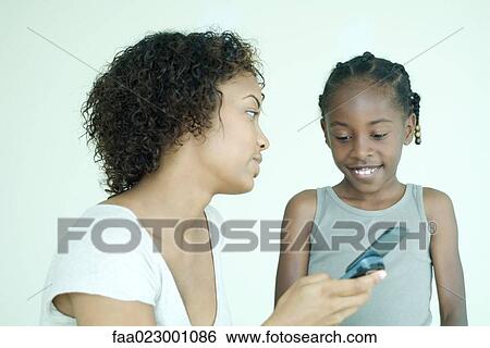 Stock Photograph - Mother and daughter using cell phone together, smiling. Fotosearch