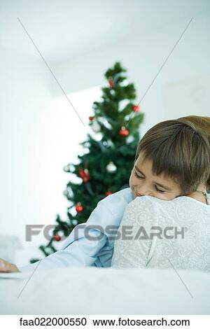 Mother sitting on sofa, holding boy in arms, Christmas tree in background, boy smiling View Large Photo Image Stock Image - Mother sitting on sofa, holding boy in arms, Christmas tree in background, boy smiling. Fotosearch