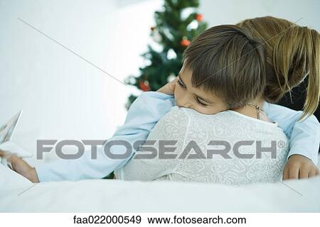 Stock Photo - Mother sitting on sofa, holding boy in arms, Christmas tree in background, boy holding star. Fotosearch