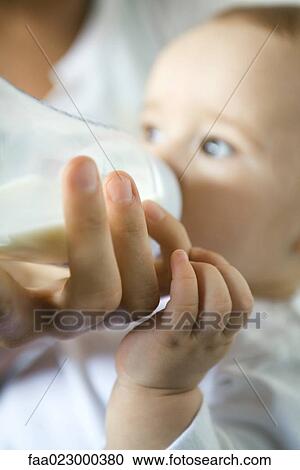 Stock Image - Mother's hand holding bottle while baby drinks, close-up. Fotosearch