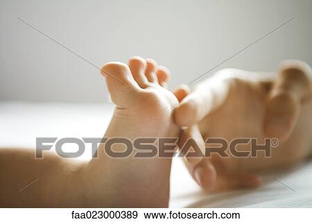 Stock Photo - Mother's hand tickling baby's foot, close-up. Fotosearch