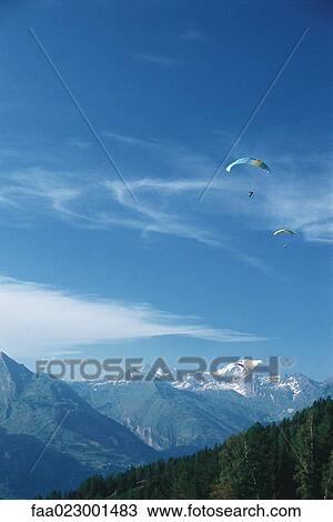 Stock Image - Paragliders in mountainous landscape. Fotosearch