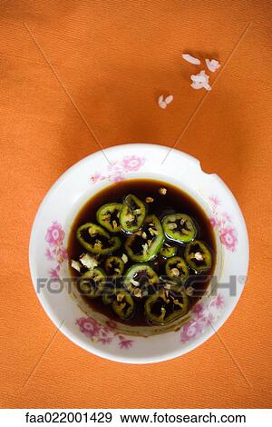 Stock Photo - Plate of peppers in sauce, grains of rice of tablecloth, high angle view. Fotosearch