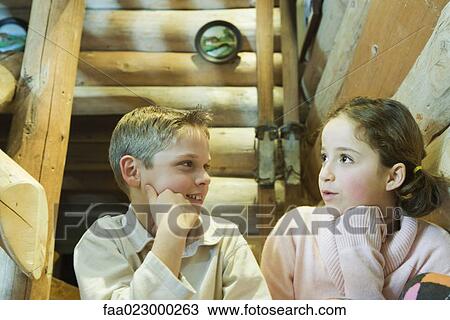Stock Image - Preteen boy and girl sitting side by side, talking. Fotosearch