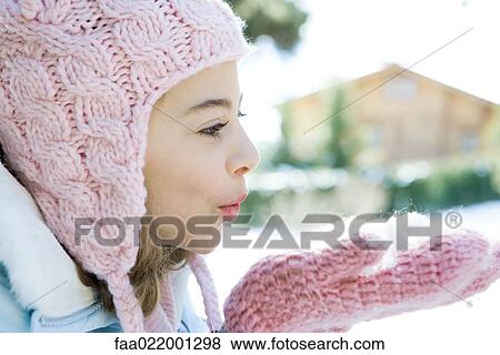 Stock Photo - Preteen girl blowing handful of snow in mittens, side view. Fotosearch