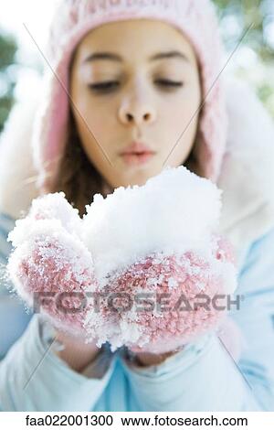 Stock Image - Preteen girl holding handful of snow in mittens, blowing. Fotosearch