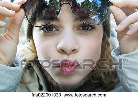 Stock Image - Preteen girl lifting sunglasses, puckering at camera, close-up. Fotosearch