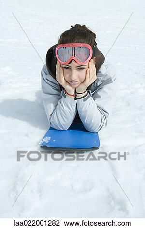 Stock Image - Preteen girl lying on snowboard in snow, portrait. Fotosearch