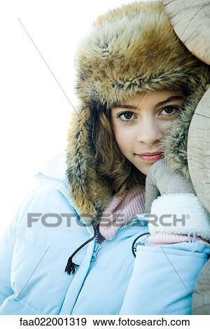 Stock Photo - Preteen girl wearing fur hat and winter jacket, smiling at camera, portrait. Fotosearch