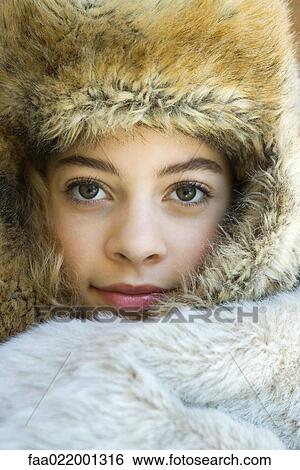 Stock Photograph - Preteen girl, wearing fur hat, wrapped in fur blanket, looking at camera, close-up portrait. Fotosearch