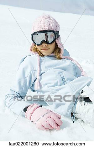 Stock Image - Preteen girl wearing ski gear, reclining in snow, portrait. Fotosearch
