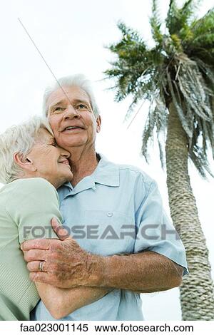 Stock Photography - Senior couple smiling and nuzzling, palm tree in background, low angle view. Fotosearch